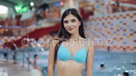 穿蓝色泳衣的年轻女人在游泳池里摆姿势水上公园里一个漂亮女孩看镜头的肖像视频的预览图