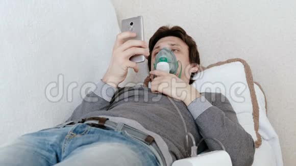 使用雾化器和吸入器进行治疗年轻人通过吸入面罩吸入躺在沙发上聊天视频的预览图