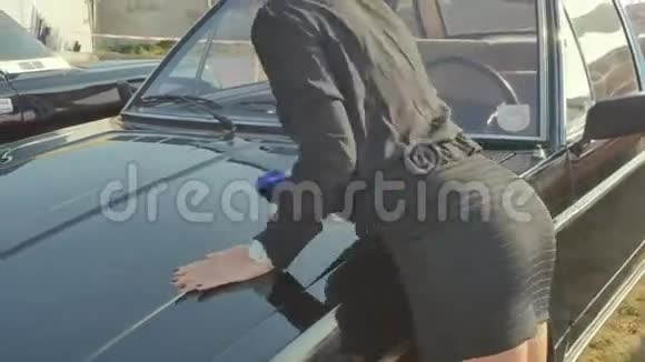 戴墨镜的漂亮女人清洗黑色复古车的引擎盖视频的预览图