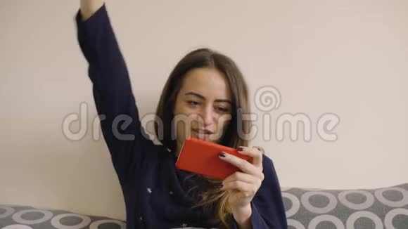 快乐年轻的女人在智能手机上玩游戏躺在家里的床上视频的预览图
