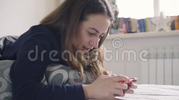 年轻女子在智能手机上玩游戏躺在家里的床上视频的预览图