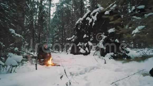 坐在篝火前树林里的年轻人试图取暖视频的预览图