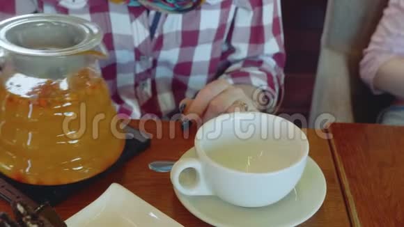 一个白人女人的手把沙棘茶从透明茶壶倒入白色的杯子里近距离观看视频的预览图