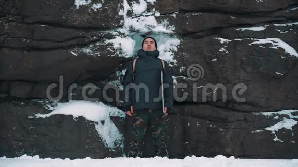 年轻人在雪覆盖的岩壁前沉思视频的预览图