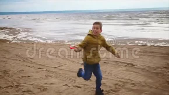 一个快乐的男孩手里拿着风筝飞快地穿过海边的沙滩视频的预览图