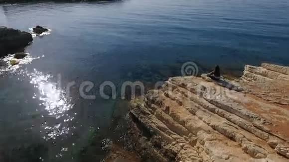 女人坐在悬崖上的石头上欣赏着美丽的海景视频的预览图