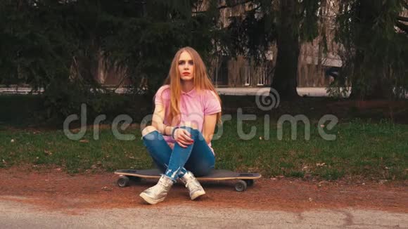 夏季公园日出时姜红发女人坐在长板滑板上视频的预览图