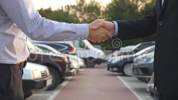 两个商人互相握手车停在后台经理或经销商之间的握手视频的预览图