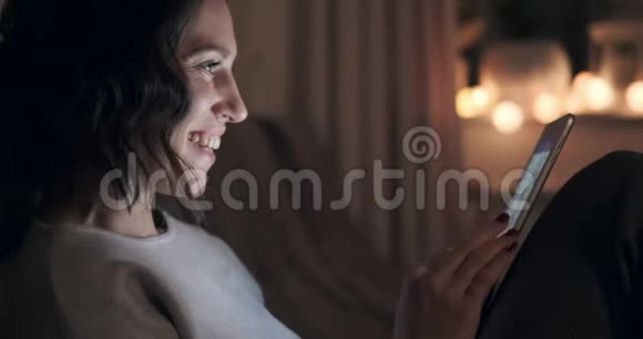 快乐的女人晚上用数码平板电脑视频的预览图