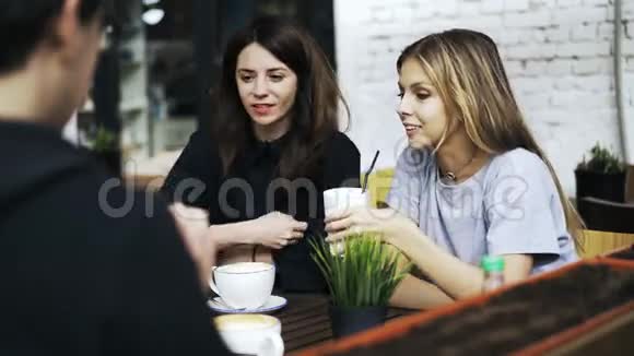 两个女孩和一个男人坐在外面的咖啡馆里一边说话一边打手势视频的预览图