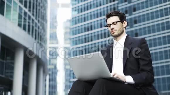一位年轻英俊的商人在外面用笔记本电脑工作视频的预览图