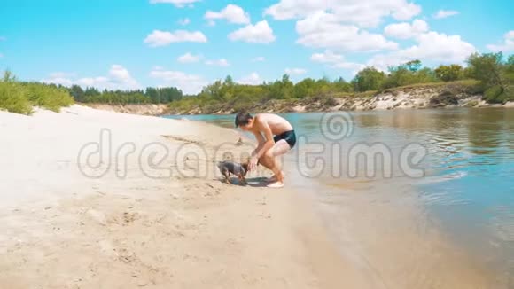 少年抚摸着一条湿狗在沙滩上靠近河水的慢动作视频少年男孩夏天洗澡视频的预览图