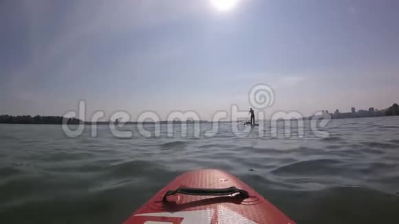 在冲浪板上划船太阳背景上的SUP板日出男人在城市的SUP板上划桨视频的预览图