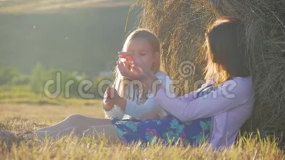 妈妈和女儿在日落时坐在稻草堆上母亲和她的小女儿在户外野外玩得很开心这就是视频的预览图