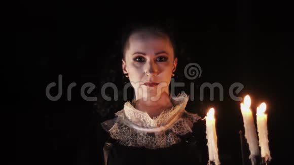 神秘的女人穿着维多利亚式的裙子在黑暗的房间里看着烛台视频的预览图