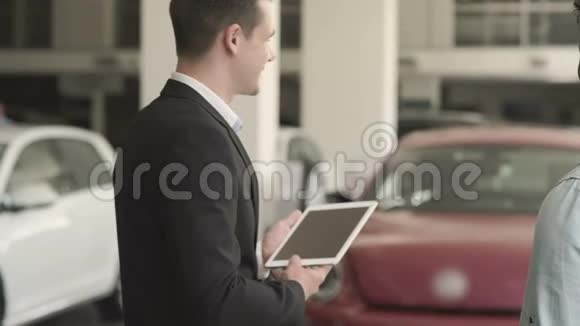 经理带着平板电脑在汽车陈列室向顾客展示汽车视频的预览图