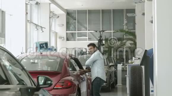 快乐的黝黑男人在汽车附近跳舞在汽车经销店里竖起大拇指视频的预览图