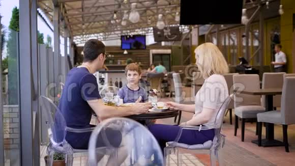 一个年轻的家庭在一家餐馆吃饭一个女人被她的丈夫拍照她喝茶他们的孩子喝一杯视频的预览图
