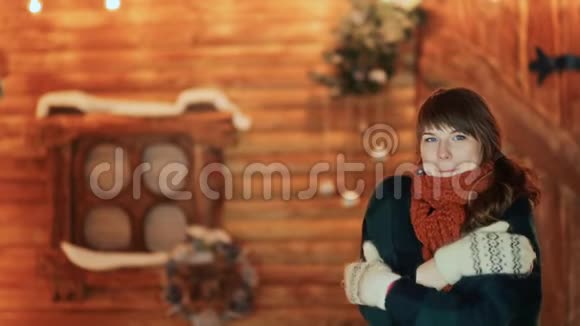 一个穿着手套的冻僵的女孩在一座木制童话般的房子的背景下温暖自己圣诞节和新年主题视频的预览图