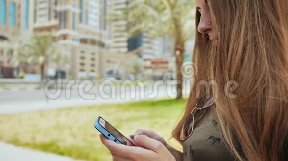 在迪拜的城市街道背景下女孩在智能手机上拨打一个号码或信息视频的预览图