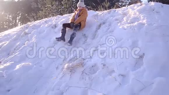 快乐的少女在白雪覆盖的森林背景下的冬季公园里带着雪滚下山寒冷的晴天视频的预览图