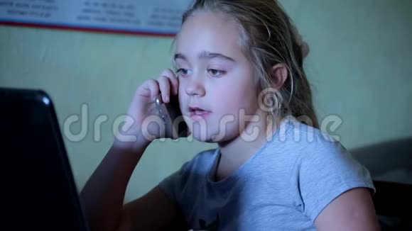 可爱的小女孩坐在电脑前用手机说话对小工具的依赖视频的预览图