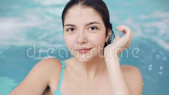 穿着蓝色泳衣在泳池里摆着绿松石水的年轻女子视频的预览图