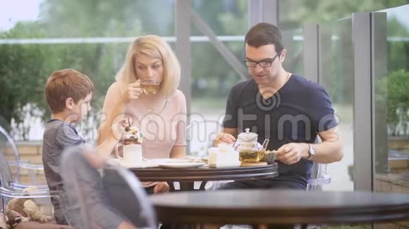 一个普通的家庭在一家餐馆吃饭父亲喝热茶儿子忙着吃巧克力奶昔和视频的预览图