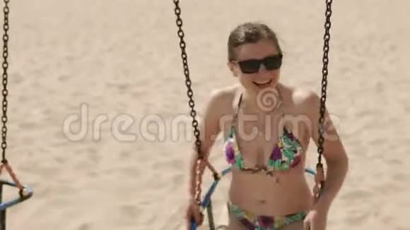 穿着泳衣和太阳镜在海滩上荡秋千的年轻女孩视频的预览图