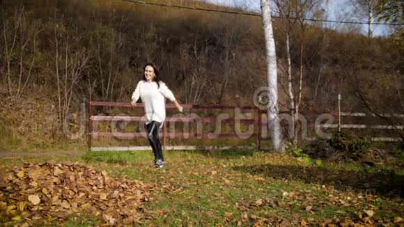 一个女人在秋天踢树叶到处都是女孩踢在一堆干燥的秋叶上4k60fps视频的预览图