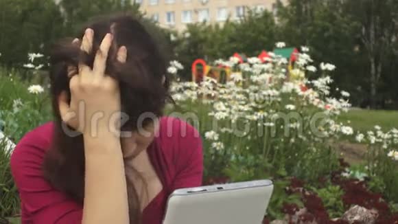 年轻的黑发女人抑郁症使用平板电脑旁边的雏菊在公园视频的预览图