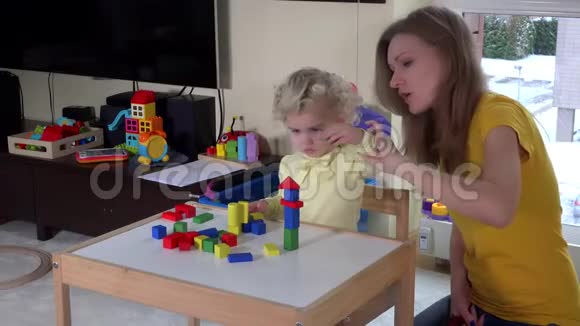 可爱的女孩和妈妈在家的小桌子附近玩五颜六色的木砖视频的预览图