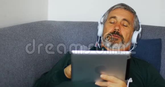 躺在沙发上的人在数码平板电脑上听音乐视频的预览图