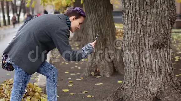 一个女人正在手机上拍摄树木和树叶的照片社交网络照片视频的预览图