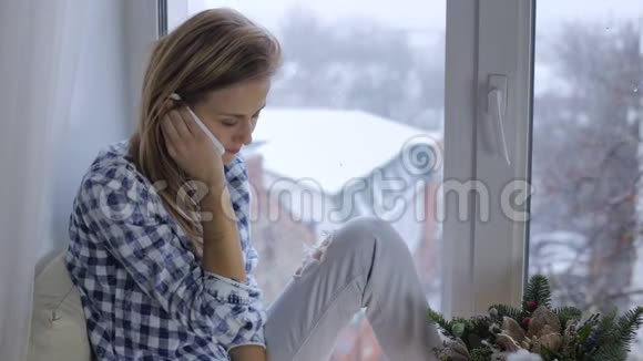 年轻女子在窗台上靠窗打电话视频的预览图