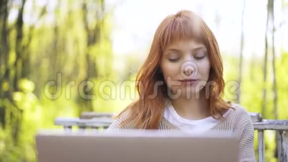 一位红头发的年轻女子在公园打字的正面景色视频的预览图