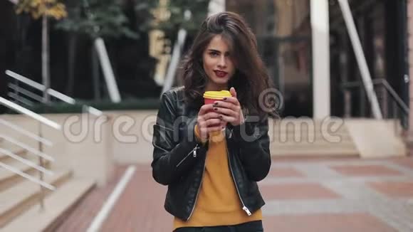 幸福的年轻女子走在商务中心附近手里拿着一杯咖啡跳舞美丽的女孩视频的预览图
