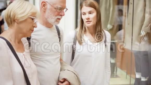 年长夫妇和他们的女儿在商场购物站在商店橱窗旁边挑选衣服视频的预览图