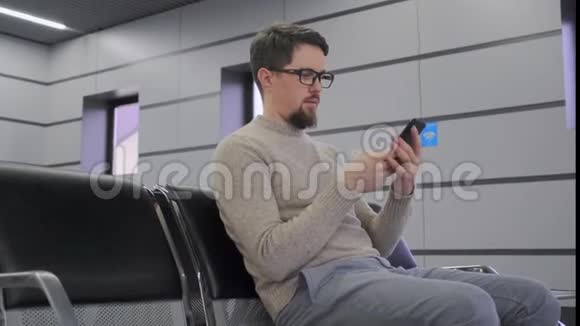 男人坐在机场用智能手机视频的预览图