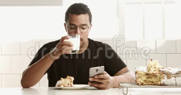 混合种族黑人男子早餐吃牛奶和蛋糕并通过电话交谈视频的预览图