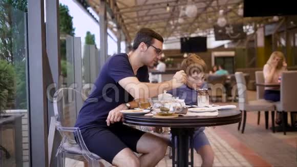 英俊的男人穿着休闲的蓝色衬衫和马裤坐在餐厅里背景是儿子和人年轻的父亲视频的预览图