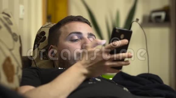 中型男子在床上用手机听音乐视频的预览图
