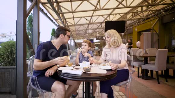 一个幸福的家庭和他们的儿子在咖啡馆的形象可爱的一对有孩子的夫妇一起在披萨店视频的预览图