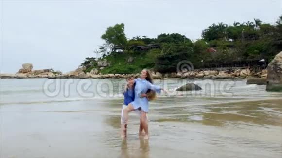 男人把女孩抱在怀里绕着她转穿着蓝色衣服的年轻夫妇在沙滩上飞视频的预览图