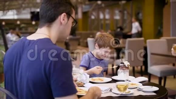 幸福的家庭和小儿子坐在桌子旁妈妈喝茶用智能手机有乐趣的男孩视频的预览图