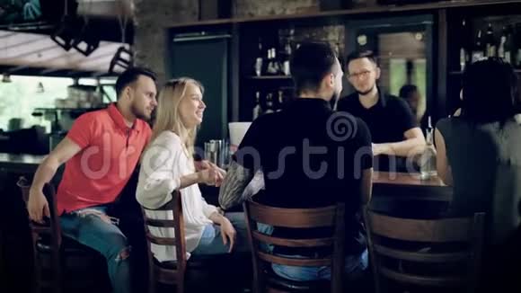 酒吧服务员在木桌的另一边工作时朋友坐在酒吧柜台前的情景视频的预览图