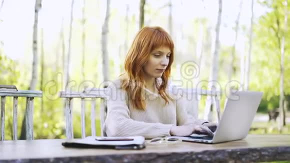一个红头发的年轻女子在公园打字视频的预览图
