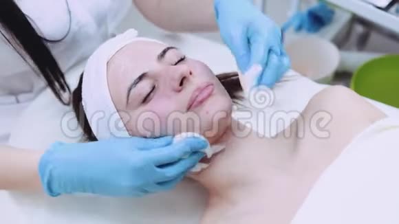 美容师从美容面具上清除美丽女人的脸复壮程序护肤照料视频的预览图