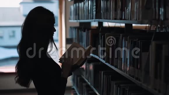 图书馆书架前一个女孩看书的剪影视频的预览图