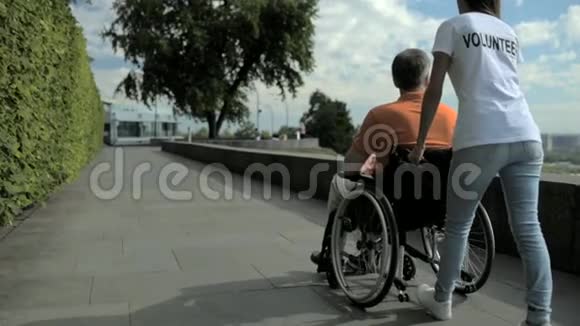 一名女性志愿者用轮椅行走的后视图视频的预览图